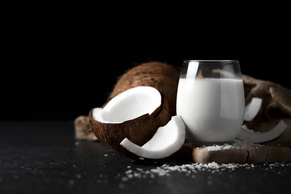 Свіже кокосове молоко в склянці на темному фоні, кокосовий косметичний крем, молочний коктейль з кокосовими скибочками — стокове фото