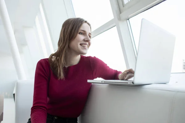 Jovem freelancer menina sentado em um café com um laptop e beber café, mulher usar um computador perto da janela — Fotografia de Stock