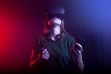 Modern sanal gerçeklik gözlüklü kız oyuncu koyu kırmızı-mavi arka planda bir tetikçiyi oynuyor, bir kadın oyun kumandalarıyla ateş ediyor