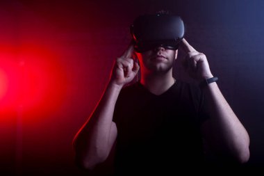 Modern kablosuz sanal gerçeklik gözlüklü bir adam karanlık bir arka plana karşı, bir adam sanal dünyaya dokunuyor.