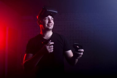 Modern sanal gerçeklik gözlüklü bir adam kablosuz joystickleri 3 boyutlu arka planda tutar.