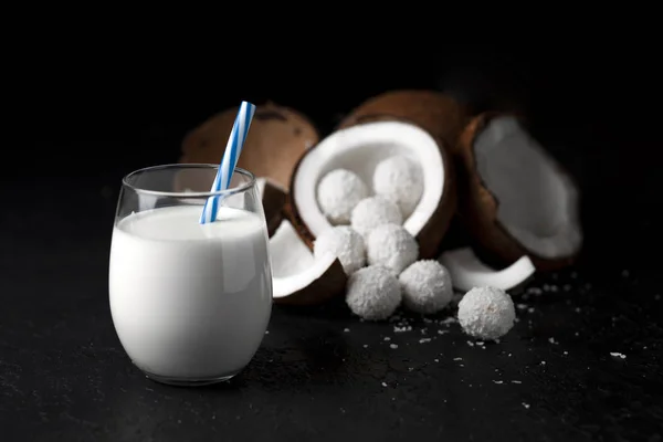 Leite de coco branco em um copo em um fundo preto escuro, doces com flocos de coco, produtos de cozinha — Fotografia de Stock