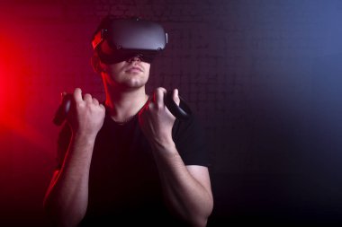 Modern sanal gerçeklik gözlüklü bir adam kablosuz joystickleri 3 boyutlu arka planda tutar.