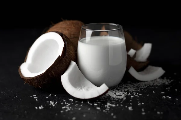 fresh coconut milk in a glass against a dark background, coconut cosmetic cream, milkshake with coconut slices