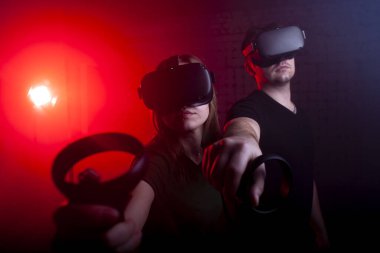 Modern kablosuz sanal gerçeklik ve joystickler gözlüklü iki oyuncu oyun odasında bir tetikçiyi oynuyorlar, bir adam ve bir kız sanal dünyada.