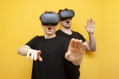Modern VR gözlüklü iki adam sarı arka planda oynuyorlar. Sanal gerçeklik gözlüklü iki oyuncu arkadaş.