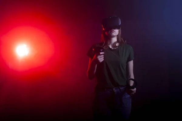 girl gamer stands in a virtual reality game room and holds VR devices, a woman plays a shooter at night