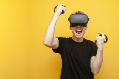 VR gözlüklü duygusal adam sanal bir oyun kazanıyor, bir oyuncu sarı arka plana karşı zafer kazanıyor.