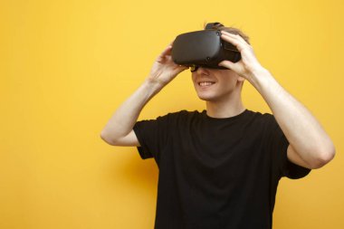 Sarı arka planda VR gözlüklü adam bir cihaz tutuyor ve gülümsüyor, bir oyuncu oyuna başlıyor ve sanal gerçeklik gözlüğü takıyor.