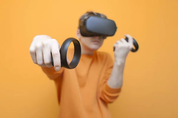 Mann mit Brille auf orangefarbenem Hintergrund, ein Spieler hält Steuerknüppel und spielt einen virtuellen Shooter — Stockfoto
