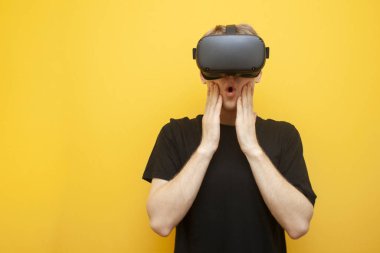 Sarı arka planda VR gözlüklü, modern sanal gerçeklik aletleri kullanan şaşırmış bir adam.