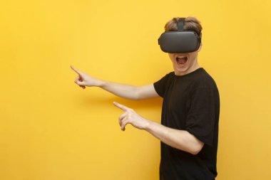 Sarı arka planda VR gözlüklü bir oyuncu bir cihaz tutuyor ve parmaklarını mesaj için bir yeri işaret ediyor. Sanal gerçeklik için kablosuz cihazları olan bir adam.