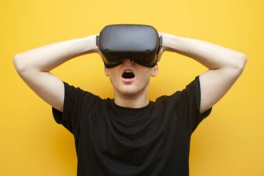 Sarı arka planda VR gözlüklü genç adam korku ve çığlıklara bakıyor, adam sanal gerçeklik gözlüğü kullanıyor ve korkuyor.
