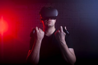 VR gözlüklü ciddi vahşi adam sanal gerçeklik odasında duruyor ve joysticklerle, erkek oyuncularla, sanal dünyayla oynuyor