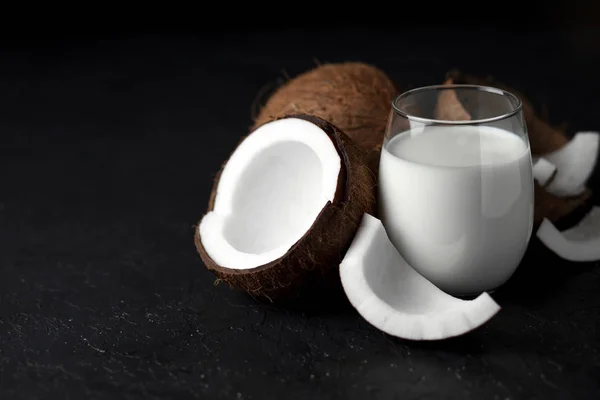 Leche de coco fresca en un vaso sobre un fondo oscuro, crema cosmética de coco, batido con rodajas de coco — Foto de Stock