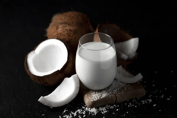 Свежее кокосовое молоко в стакане на темном фоне, кокосовые косметические сливки, молочный коктейль с кокосовыми ломтиками — стоковое фото