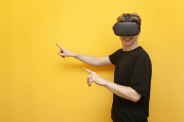 Sarı arka planda VR gözlüklü bir oyuncu bir cihaz tutuyor ve parmaklarını mesaj için bir yeri işaret ediyor. Sanal gerçeklik için kablosuz cihazları olan bir adam.