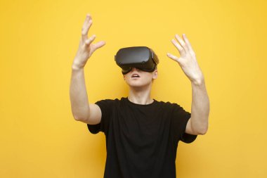 Sanal gerçeklik cihazları kullanarak sarı arka plandaki sanal alana dokunan sanal gözlüklü şaşırmış bir adam.