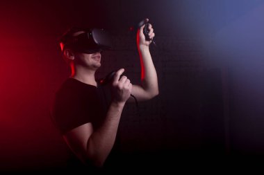 guy a gamer in modern glasses of virtual reality plays a shooter, a man is focused on a 3D game in a dark room