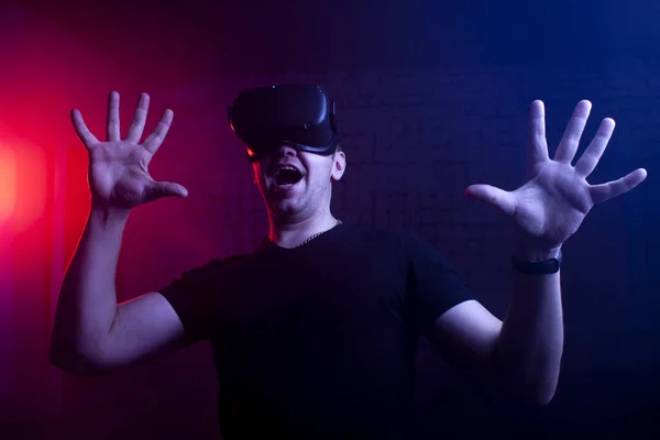 scared guy a gamer in a virtual reality game room, a man screams in VR glasses and plays a shooter
