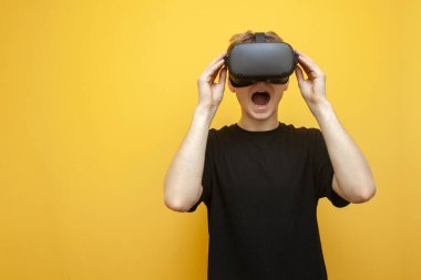 Sarı arka planda VR gözlüklü genç adam korku ve çığlıklara bakıyor, adam sanal gerçeklik gözlüğü kullanıyor ve korkuyor.