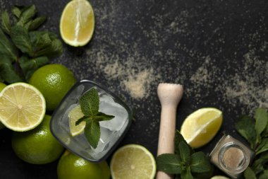 Ev yapımı kokteyl hazırlama süreci, siyah arka planda mojito malzemeleriyle dolu, ferahlatıcı bir yaz kokteyli.