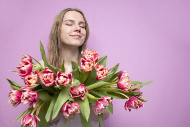 Genç ve güzel bir kız pembe arka planda bir buket çiçek tutuyor, laleli mutlu bir kadın.,