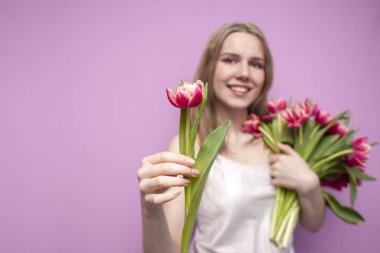 Çekici kız pembe arka planda bir buket çiçek tutar ve bir lale verir, satıcı çiçek verir, bir kadın lale verir.