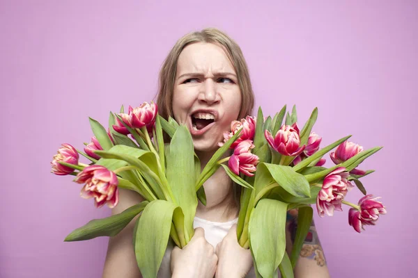 Young beautiful girl with a bouquet of flowers on a colored pink background, a woman holds tulips and screams from happiness — 스톡 사진