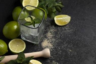 Ev yapımı kokteyl hazırlama süreci, siyah arka planda mojito malzemeleriyle dolu, ferahlatıcı bir yaz kokteyli.