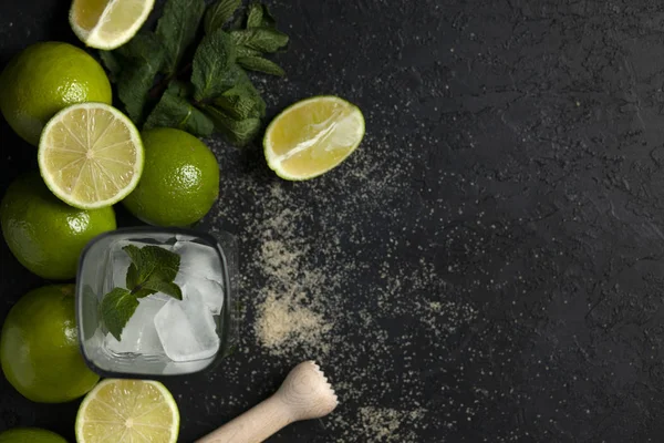 Ev yapımı kokteyl hazırlama süreci, siyah arka planda mojito malzemeleriyle dolu, ferahlatıcı bir yaz kokteyli.