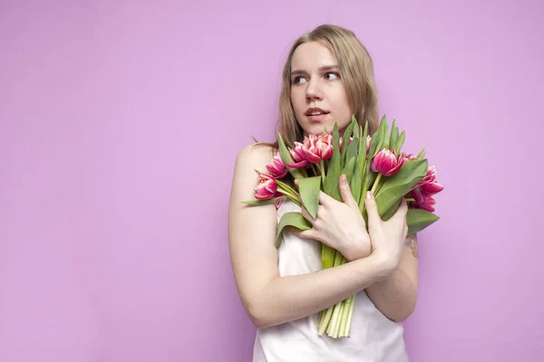 Young beautiful girl with a bouquet of flowers on a colored pink background, a woman holds tulips and smiles — 스톡 사진