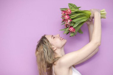 Kız pembe arka planda bir buket çiçek tutuyor ve kokluyor, laleli güzel bir kadın.