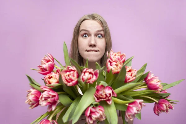Emotional face of a girl in flowers on a pink background, a surprised woman with a bouquet of tulips is smiling — 스톡 사진