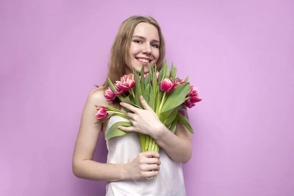 Junges schönes Mädchen mit einem Blumenstrauß auf farbigem rosa Hintergrund, eine Frau hält Tulpen und lächelt — Stockfoto
