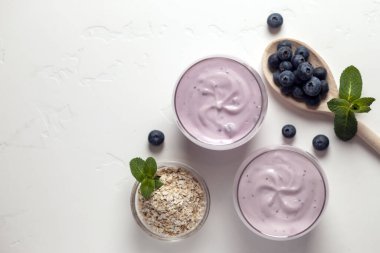 Beyaz dokuma masasında yaban mersinli ve tahıllı iki taze yaban mersinli yoğurt.