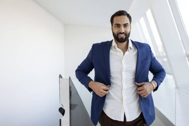 Successful handsome businessman in a blue suit at the workplace looks out the window, portrait of a manager at work