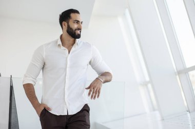 Portrait of a successful handsome man in a white shirt in the morning in a white building, businessman looks out the window