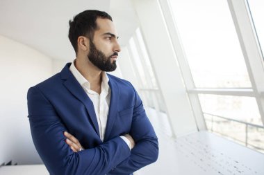 Yakışıklı, başarılı bir şirket yöneticisi beyaz bir ofiste duruyor ve pencereden dışarı bakıyor. İş yerindeki bir iş adamının portresi.