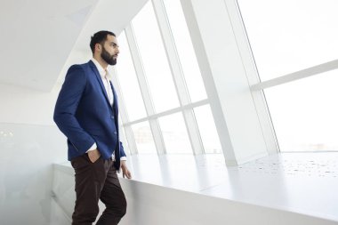 Yakışıklı, başarılı bir şirket yöneticisi beyaz bir ofiste duruyor ve pencereden dışarı bakıyor. İş yerindeki bir iş adamının portresi.