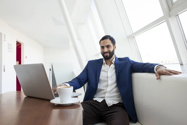 Joven empresario de éxito utilizar un ordenador portátil y tomar café por la mañana en el trabajo, un freelancer está sentado con una computadora en un café blanco — Foto de Stock