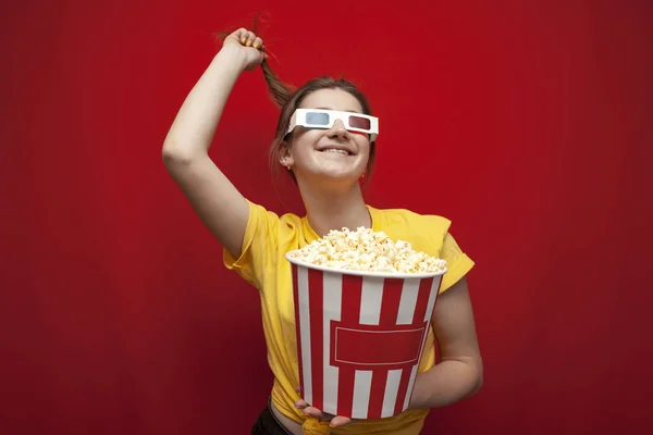 Funny happy young girl in 3D glasses and with popcorn on a red background, a student watching a 3D film — Stok fotoğraf