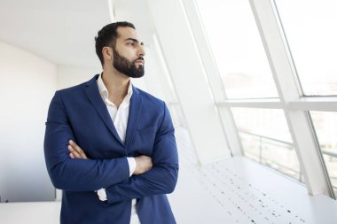 Yakışıklı, başarılı bir şirket yöneticisi beyaz bir ofiste duruyor ve pencereden dışarı bakıyor. İş yerindeki bir iş adamının portresi.
