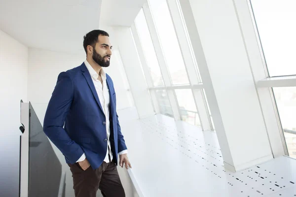 Apuesto gerente de la empresa de éxito se encuentra en una oficina blanca y mira por la ventana, retrato de un hombre de negocios en el lugar de trabajo — Foto de Stock