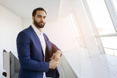 Successful handsome businessman in a blue suit at the workplace looks out the window, portrait of a manager at work, copy space