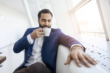 Takım elbiseli başarılı bir iş adamı bir kafede oturur, kahve içer ve pencereden dışarı bakar.