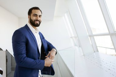 Successful handsome businessman in a blue suit at the workplace looks out the window, portrait of a manager at work, copy space