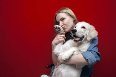 Mutlu neşeli güzel kız kırmızı arka planda bir köpeğe sarılıyor, bir kadın Golden Retriever köpeğini öpüyor, evcil hayvanları seviyor, kopyalama alanı