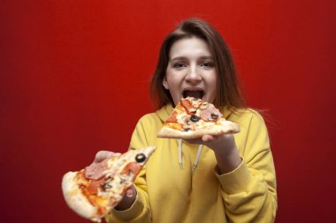 Genç ve mutlu bir kız renkli arka planda pizza yiyor, bir genç iki dilim pizza tutuyor ve fast food yiyor, uzayı kopyalıyor.