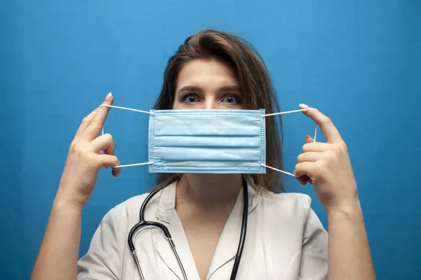 Ung Flicka Sjuksköterska Sätter Virusmask Blå Bakgrund Skydd Coronavirus Epidemin — Stockfoto